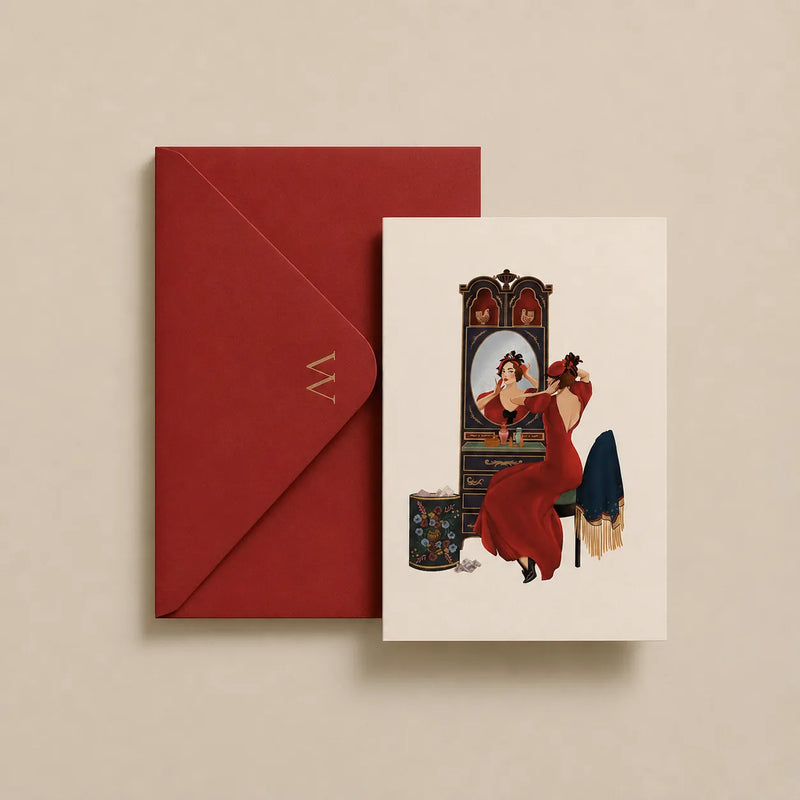 A red envelope with a gold monogram 'M' and a matching art print card featuring an Art Deco illustration of a woman in a red gown looking in a mirror, displayed on a beige background.